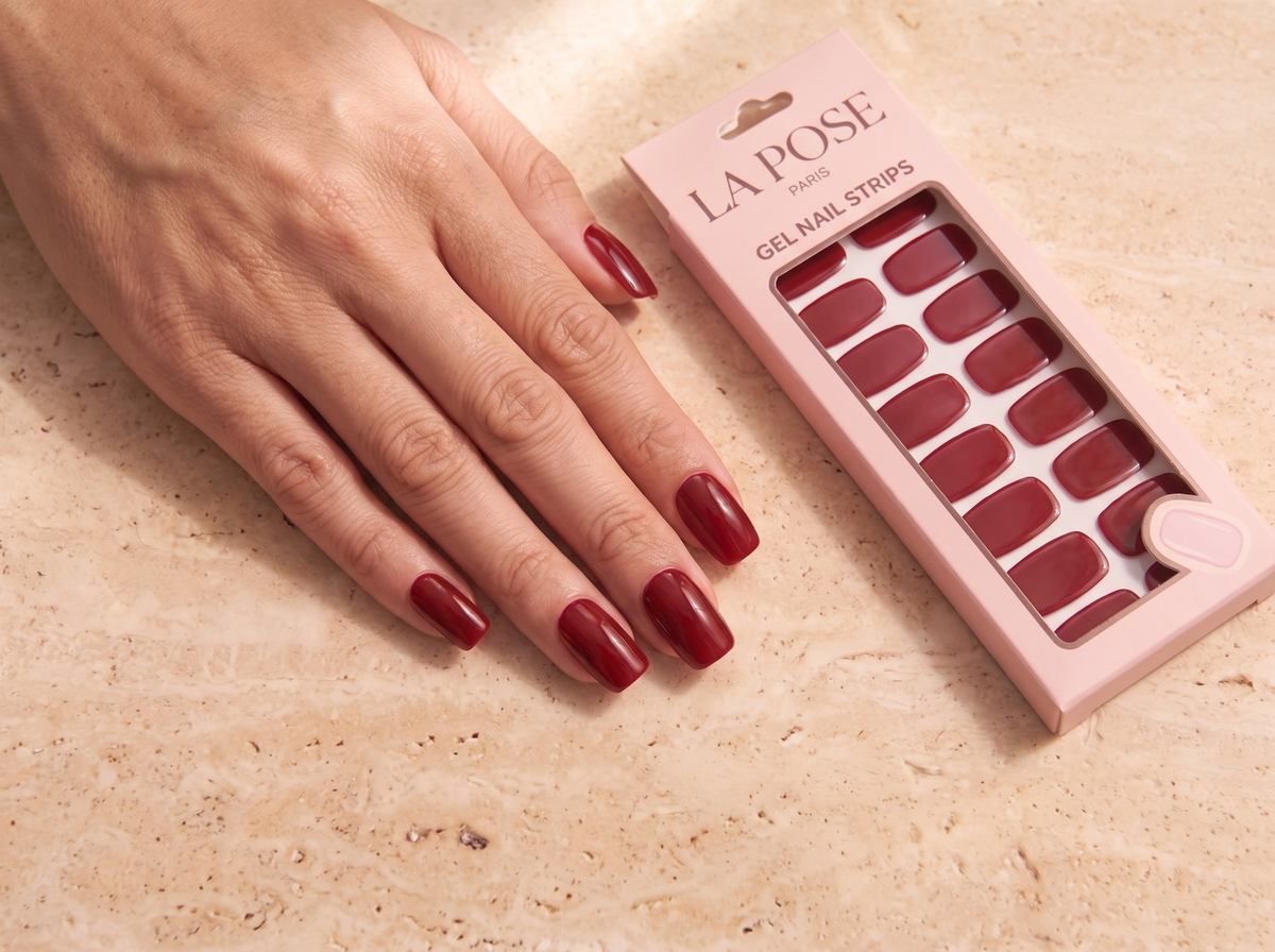 La Pose red manicure beside its closed blush carton on pale stone.